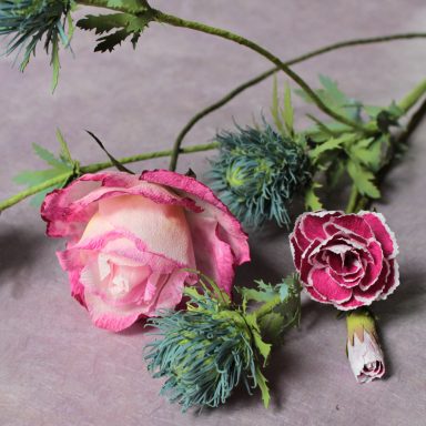 Zwei samtige Rosen in Rosa und eine kleine, bunte Blume auf einem grauen Hintergrund.